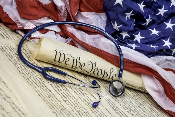 The United States Constitution rolled up on an American flag with a medical stethoscope symbolizing the need for good healthcare